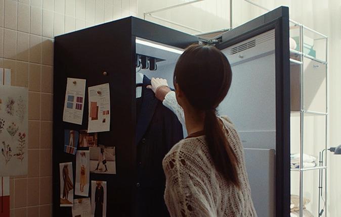 LG 스타일러에서 문을 열고 검은색 옷을 꺼내고 있는 여자가 있습니다.