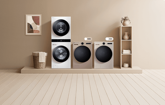 엷은 브라운톤의 실내에 워시타워가 놓여있습니다. 그 주변에 테이블, 수납장, 세탁바구니가 배치되어 있고 벽에는 그림 액자가 걸려있습니다.