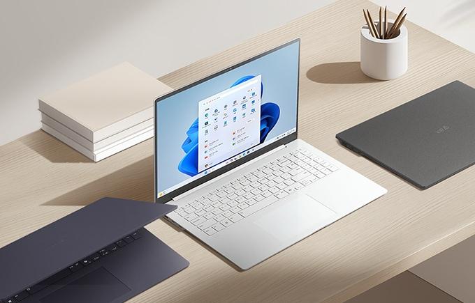 밝은 책상 위에 다양한 색상의 노트북 3대와 책, 연필꽂이가 정돈된 상태로 놓여 있습니다.