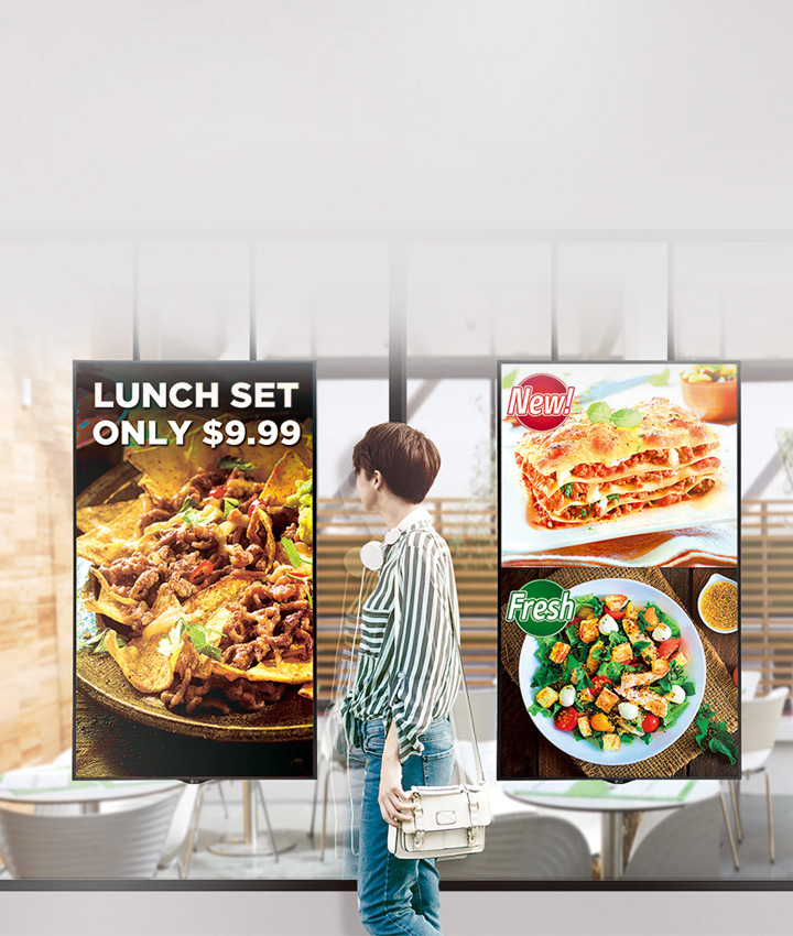 한 여성이 식당 앞을 지나가고 있으며, 창문에는 음식 광고가 붙어 있습니다. 광고에는 LUNCH SET ONLY $9.99라는 문구와 함께 나초와 고기가 담긴 요리 이미지가 보입니다. 다른 광고에는 New!라는 문구와 함께 라자냐 이미지가 있으며, Fresh라는 문구와 함께 샐러드 이미지도 있습니다. 식당 내부는 나무 테이블과 의자가 놓여 있는 모습입니다.