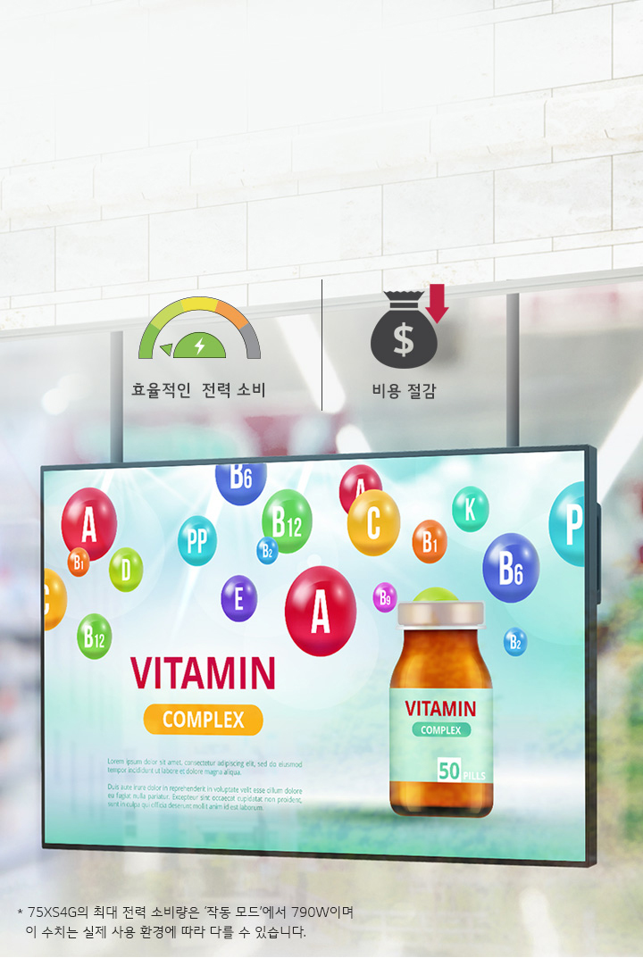 한 남성이 대형 스크린을 보고 있으며, 스크린에는 다양한 비타민 알파벳과 함께 VITAMIN COMPLEX라는 문구와 비타민 병 이미지가 보입니다. 상단에는 효율적인 전력 소비와 비용 절감이라는 문구가 각각 전력 소비 게이지와 비용 절감 아이콘과 함께 있습니다. 하단에는 75XS4G의 최대 전력 소비량은 '작동 모드'에서 790W이며 이 수치는 실제 사용 환경에 따라 다를 수 있습니다.라는 설명이 있습니다. 배경은 상점 내부로 보이며 다양한 상품들이 진열되어 있습니다.