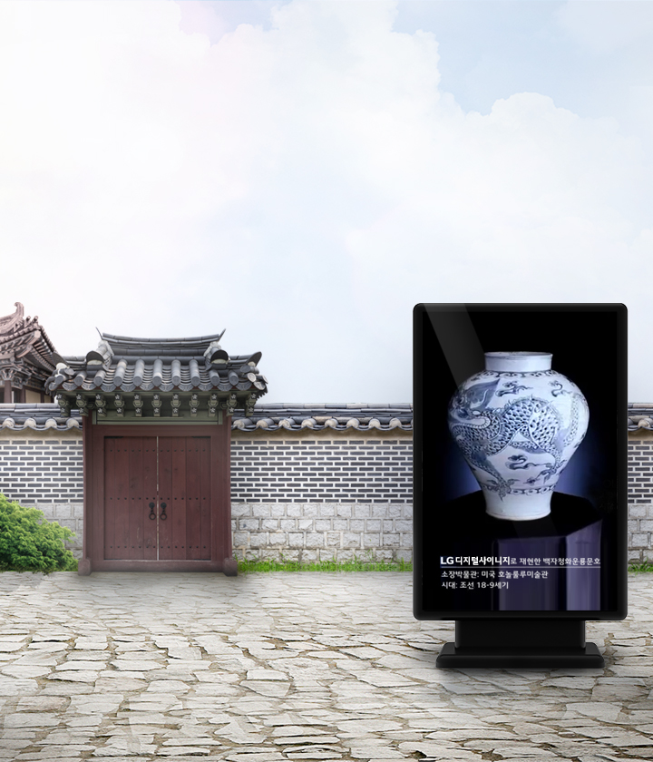 전통적인 한옥 건축물과 돌담이 있는 배경 앞에 디지털 사이니지가 설치되어 있습니다. 사이니지에는 백자 항아리 이미지가 표시되어 있으며, 아래에는 LG 디지털사이니지로 재현한 백자청화용문호 소장박물관: 미국 호놀룰루미술관 시대: 조선 18-19세기라는 텍스트가 포함되어 있습니다. 주변에는 나무와 푸른 하늘이 보입니다.