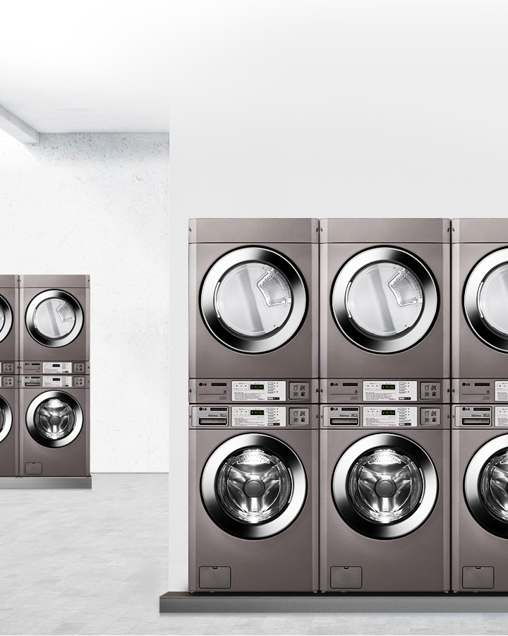 세탁기와 건조기가 나란히 배치된 세탁실의 모습입니다. 각 기기는 금속성 외관을 가지고 있으며, 디지털 디스플레이와 버튼이 있는 조작 패널이 보입니다. 배경은 밝은 색상의 벽과 바닥으로 구성되어 있습니다.