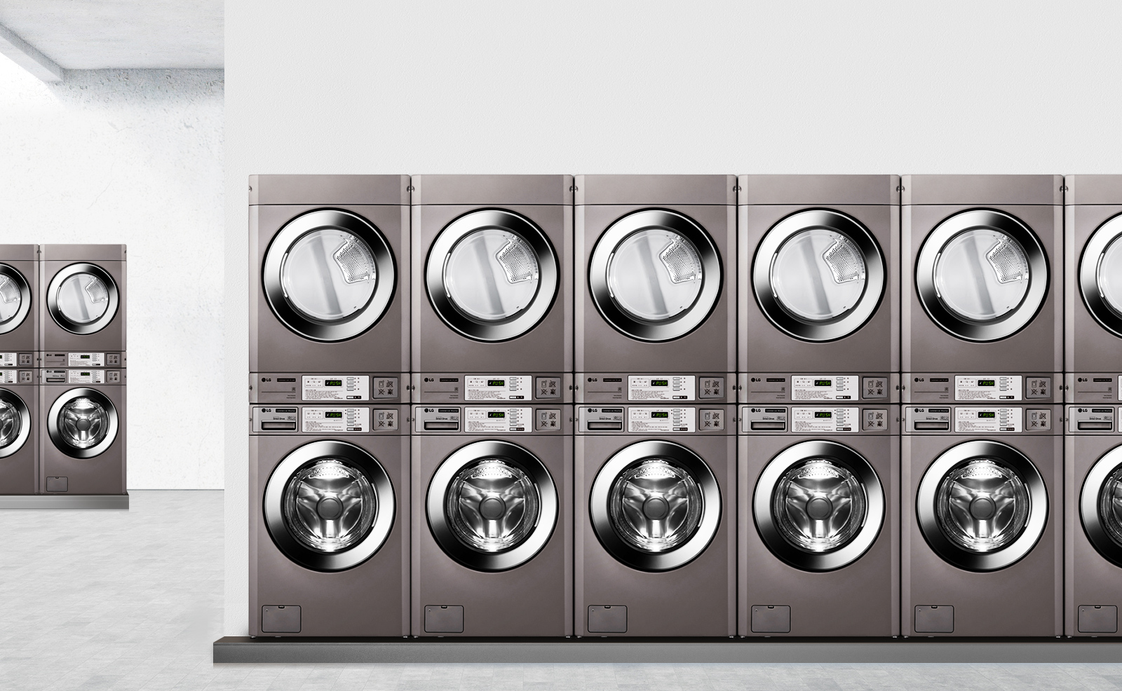 세탁기와 건조기가 나란히 배치된 세탁실의 모습입니다. 각 기기는 금속성 외관을 가지고 있으며, 디지털 디스플레이와 버튼이 있는 조작 패널이 보입니다. 배경은 밝은 색상의 벽과 바닥으로 구성되어 있습니다.