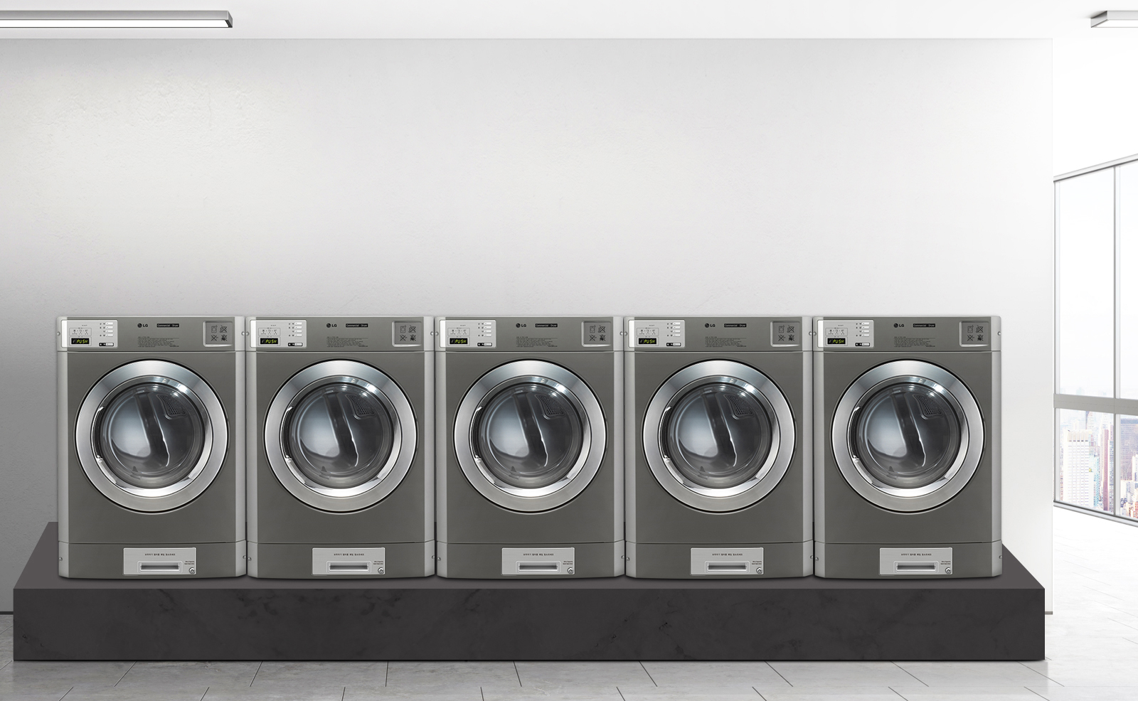 회색 벽 앞에 다섯 대의 산업용 세탁기가 나란히 놓여 있습니다. 세탁기들은 금속성의 외관을 가지고 있으며, 각각의 문은 투명한 원형 창으로 되어 있습니다. 세탁기 상단에는 조작 패널이 있으며, 디지털 디스플레이와 버튼들이 보입니다. 바닥은 대리석 타일로 되어 있습니다. 창문을 통해 도시 풍경이 보입니다.