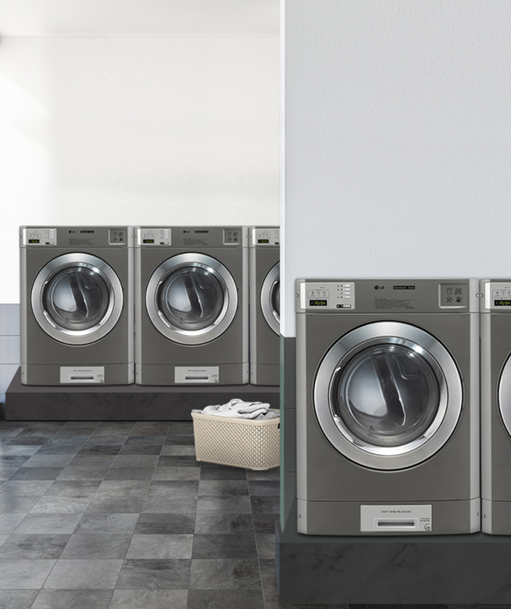 세탁기가 여러 대 놓여 있는 세탁실의 모습입니다. 세탁기 앞에는 빨래 바구니가 놓여 있으며, 바닥은 타일로 되어 있습니다. 세탁기 상단에는 디지털 디스플레이와 조작 버튼이 보입니다. 실내는 밝은 조명으로 환하게 비춰지고 있습니다.