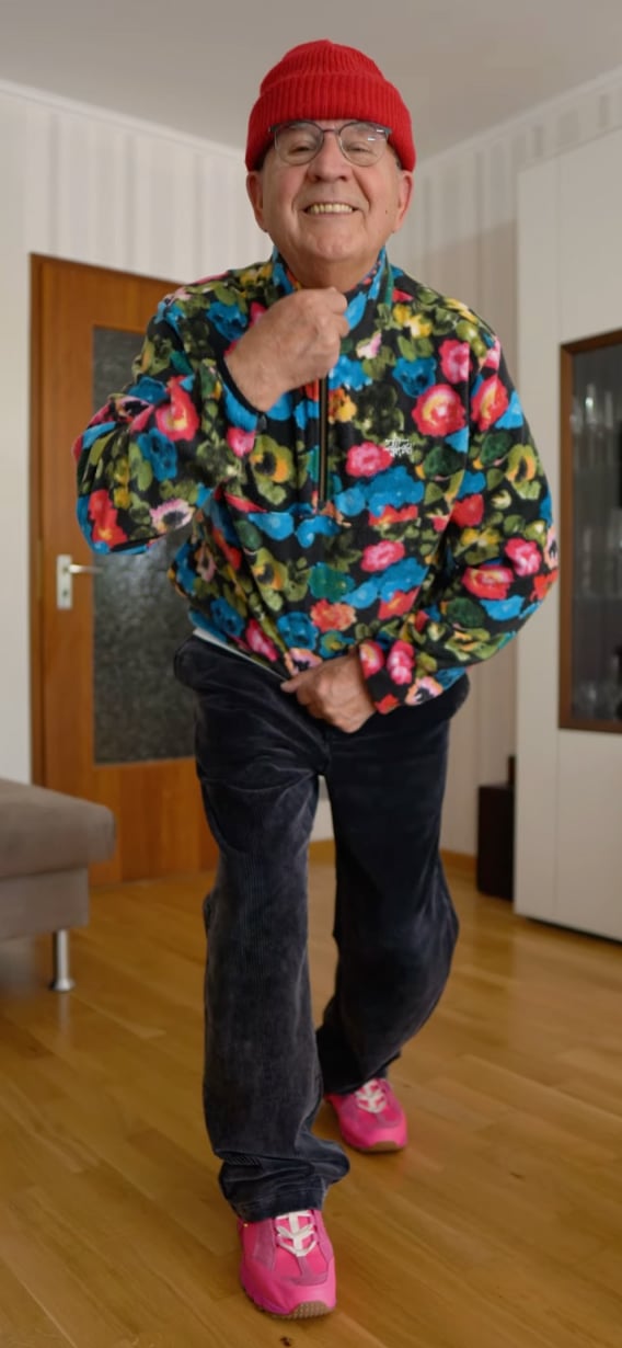 다채로운 색상의 자켓을 입고 빨간 모자를 쓴 남성이 밝게 웃으며 포즈를 취하고 있습니다.