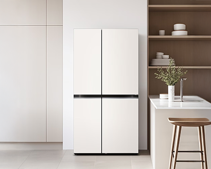 좌측에는 베이지색 수납장, 우측에는 우드 선반과 아일랜드 식탁이 있는 주방 중앙에 흰색 4도어 냉장고가 배치되어 있는 이미지