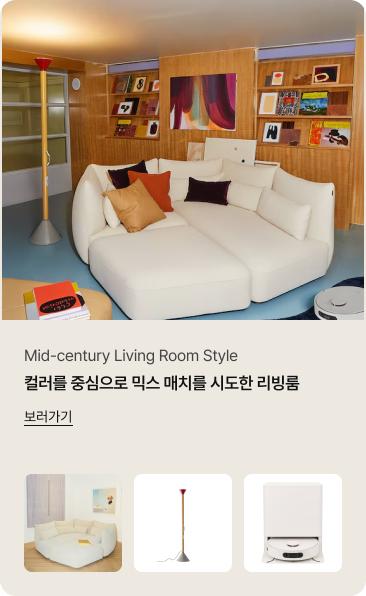 Mid-century Living Room Style. 컬러를 중심으로 믹스 매치를 시도한 리빙룸. 상세 이미지 설명: 미드센추리 모던 스타일의 거실입니다. 화이트 색상의 대형 모듈형 소파가 중앙에 배치되어 있고, 소파 위에는 오렌지색과 보라색 쿠션으로 포인트를 주었습니다. 좌측에는 빨간색 포인트가 있는 독특한 형태의 장스탠드 조명이 서 있고, 우측 하단에는 화이트 색상의 LG 로봇청소기가 충전 스테이션에 거치되어 있습니다. 배경의 우드 벽면 선반에는 다양한 책과 액자들이 전시되어 있습니다.