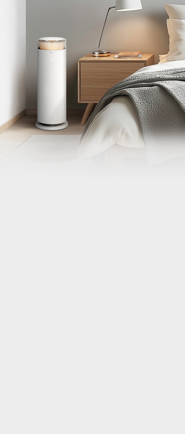 침실에 놓인 LG 퓨리케어 오브제컬렉션 하이드로에센셜 제품이 보이며, 캔들라이트 색상의 조명이 켜져 있습니다. 나무 소재의 테이블이 있으며,램프와 책이 놓여 있습니다. 흰색 침대는 회색 담요로 덮여 있습니다.