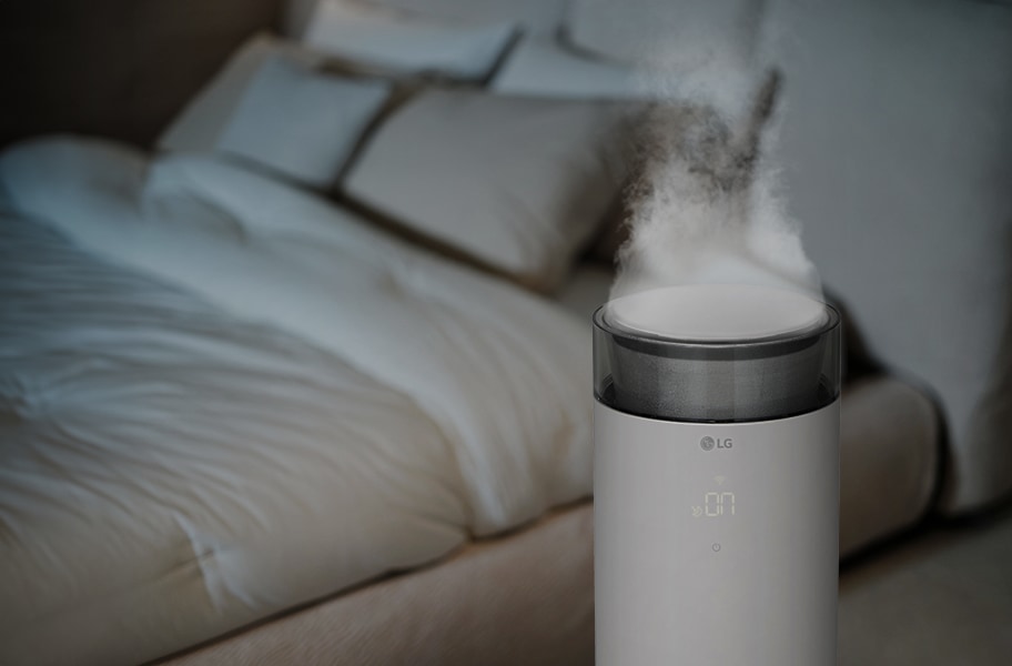 침실에 LG 퓨리케어 오브제컬렉션 하이드로에센셜 제품이 놓여 있으며, 취침 모드가 켜져 있고 가습무가 나오고 있습니다. 디스플레이에는 58%라는 숫자가 표시되어 있습니다. 침대에는 여러 개의 베개와 이불이 정돈되어 있습니다.