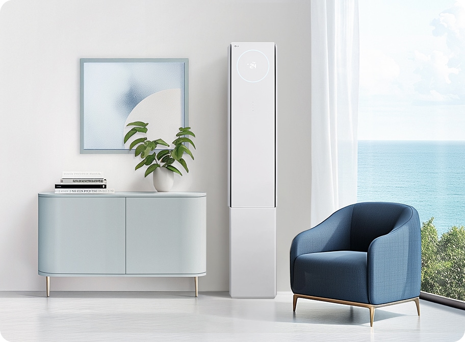 밝은 거실에 하얀색 2in1 에어컨이 설치되어 있으며, 에어컨 상단에는 24라는 숫자가 표시되어 있습니다. 에어컨 옆에는 푸른색의 안락의자가 놓여 있고, 그 옆에는 바다 풍경이 보이는 큰 창문이 있습니다. 왼쪽에는 식물이 놓인 작은 회색 수납장이 있으며, 그 위에는 두 권의 책과 함께 추상적인 그림이 걸려 있습니다.