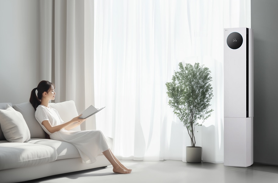 LG 휘센 AI 오브제컬렉션 뷰I 프로 에어컨이 오른쪽에 세워져 있으며, 원형 디스플레이에는 24.5°C라는 숫자가 표시되어 있습니다. 에어컨 왼쪽에는 커다란 창문이 있고, 창문을 통해 밝은 자연광이 들어오고 있습니다. 창문 앞에는 화분에 심어진 녹색 식물이 놓여 있습니다. 왼쪽에는 흰색 소파에 앉아 책을 읽고 있는 여성이 보입니다. 그녀는 흰색 원피스를 입고 있으며, 소파에는 흰색 쿠션이 놓여 있습니다.