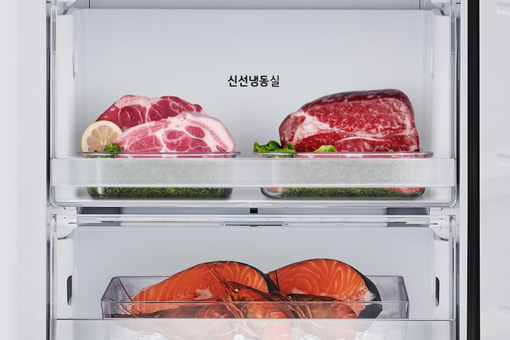 냉장고 내부에 두 개의 칸이 보이며, 위쪽 칸에는 '신선냉동실'이라는 텍스트가 있습니다. 이 칸에는 레몬 조각과 함께 놓인 두 덩어리의 고기가 담겨 있습니다. 아래쪽 칸에는 얼음 위에 놓인 연어와 바닷가재가 담겨 있습니다.