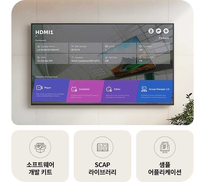 벽에_설치된_디지털_디스플레이_화면에는_hdmi1과_pc라는_제목이_있으며,_대시보드에는_여러_정보가_표시됩니다._signage_name은_lg_signage_webos3,_s/w_version은_02.72.74,_set_id는_1,_tile_mode는_off,_dpm은_on_(10_min_off),_network는_wired_connected_(192.168.0),_fail_over는_off,_play_via_url은_off로_나타납니다._화면_하단에는_contents_management라는_제목_아래_player,_scheduler,_editor,_group_manager_2.0이라는_네_가지_옵션이_있으며,_각각의_기능_설명이_포함되어_있습니다._화면_아래에는_세_개의_아이콘과_함께_소프트웨어_개발_키트,_scap_라이브러리,_샘플_어플리케이션이라는_텍스트가_있습니다._배경에는_식물이_보입니다.