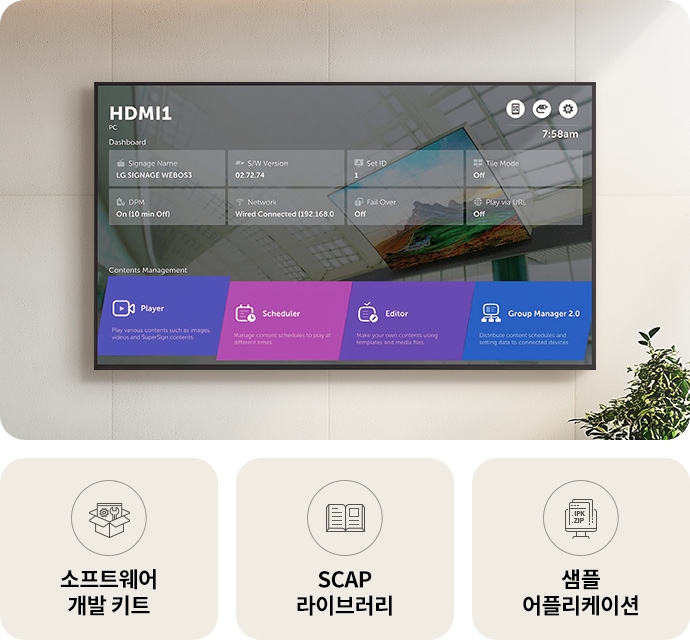 벽에_설치된_디지털_디스플레이_화면에는_hdmi1과_pc라는_제목이_있으며,_대시보드에는_여러_정보가_표시됩니다._signage_name은_lg_signage_webos3,_s/w_version은_02.72.74,_set_id는_1,_tile_mode는_off,_dpm은_on_(10_min_off),_network는_wired_connected_(192.168.0),_fail_over는_off,_play_via_url은_off로_나타납니다._화면_하단에는_contents_management라는_제목_아래_player,_scheduler,_editor,_group_manager_2.0이라는_네_가지_옵션이_있으며,_각각의_기능_설명이_포함되어_있습니다._화면_아래에는_세_개의_아이콘과_함께_소프트웨어_개발_키트,_scap_라이브러리,_샘플_어플리케이션이라는_텍스트가_있습니다._배경에는_식물이_보입니다.