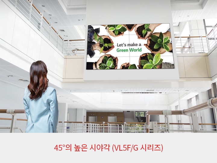 실내 공간에서 한 여성이 큰 디지털 화면을 바라보고 있습니다. 화면에는 여러 손들이 작은 화분을 들고 있으며, 