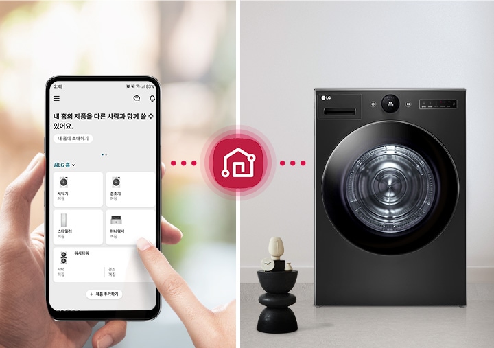 스마트폰 화면에 내 홈의 제품을 다른 사람과 함께 쓸 수 있어요.라는 문구와 함께 세탁기, 건조기, 스타일러, 에어워셔 등의 아이콘이 표시되어 있습니다. 손가락이 화면을 터치하고 있으며, 배경은 흐릿하게 처리되어 있습니다. 빨간색 점선과 집 모양의 아이콘이 중앙에 위치해 있으며, 세탁기가 놓여 있고, 그 옆에는 장식품이 올려진 작은 테이블과 소파가 있습니다.