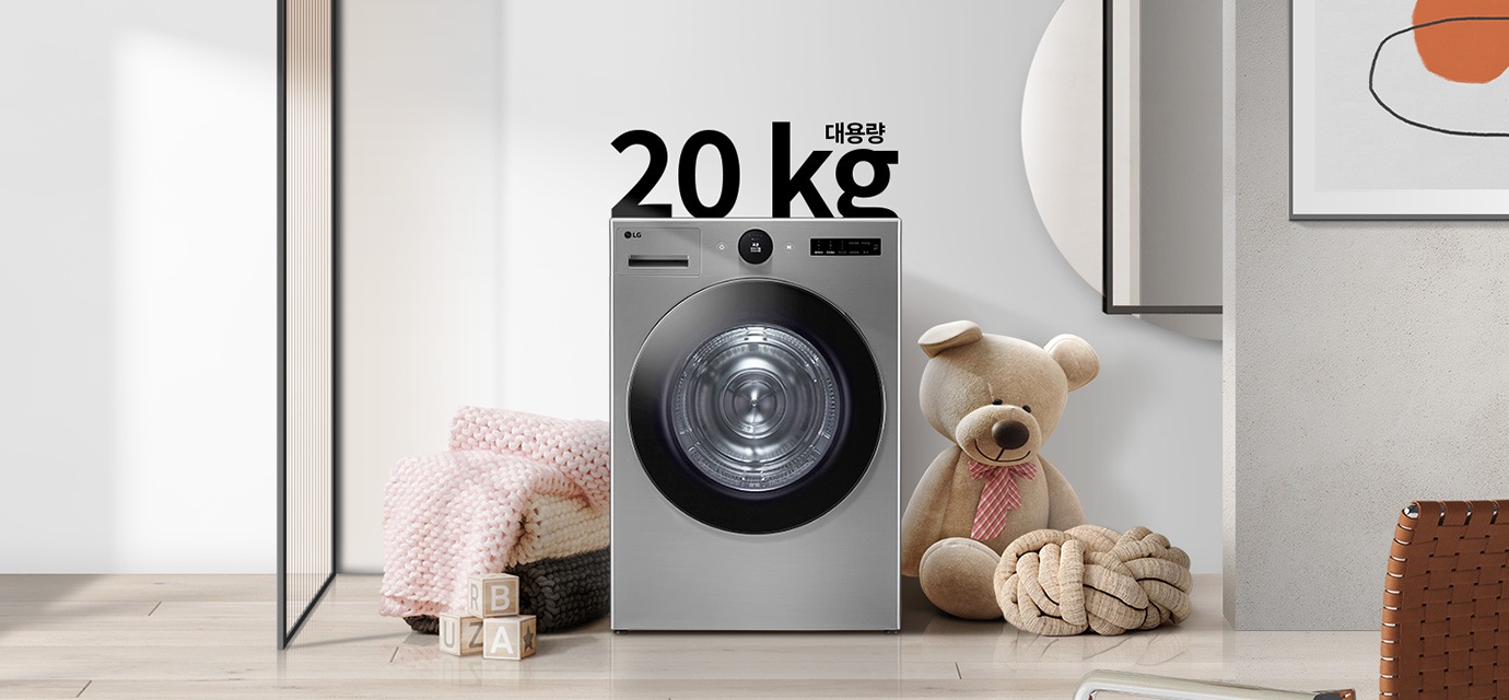 20kg 대용량 세탁기가 놓여 있으며, 주변에는 곰 인형과 장난감 블록, 그리고 핑크색 니트 담요가 보입니다. 세탁기 위에는 20kg 대용량이라는 텍스트가 있습니다. 배경은 깔끔한 실내 공간으로, 벽에는 추상적인 그림이 걸려 있습니다.