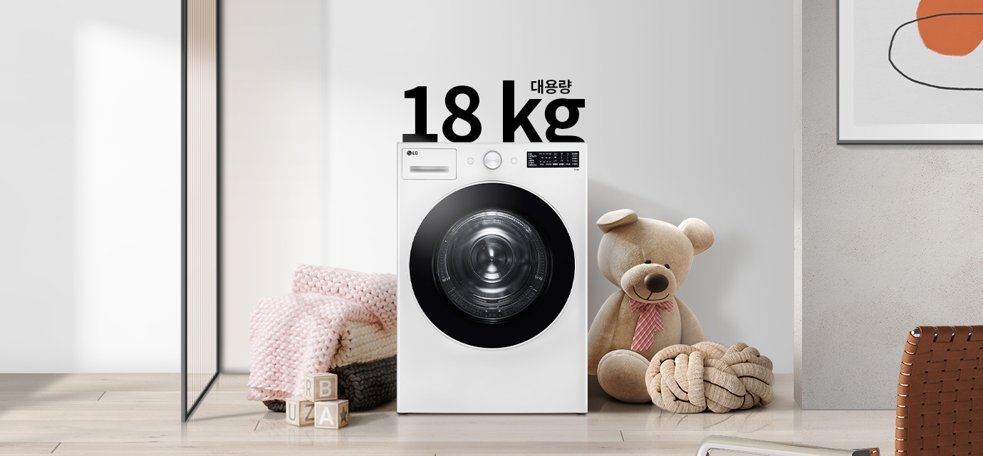 세탁기가 놓여 있으며, 18kg 대용량이라는 텍스트가 있습니다. 세탁기 옆에는 큰 곰 인형과 두꺼운 니트 담요가 놓여 있고, 바닥에는 알파벳 블록이 있습니다. 벽에는 추상적인 그림이 걸려 있습니다.