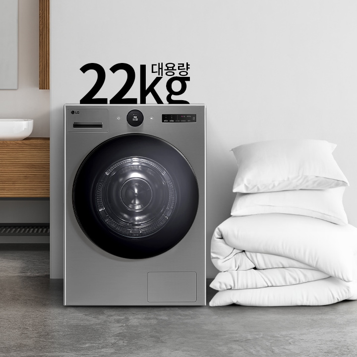 세탁기가 있으며, 22kg 대용량이라는 텍스트가 있습니다. 세탁기 옆에는 하얀색 베개와 이불이 쌓여 있고, 배경에는 세면대와 거울이 있는 욕실이 보입니다. 바닥은 콘크리트로 되어 있습니다.
