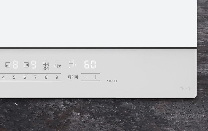 디지털 디스플레이가 있는 전자 기기의 제어 패널이 보입니다. 숫자 8, 9와 자동 감지, 터보, 타이머라는 텍스트가 표시되어 있으며, 타이머는 60으로 설정되어 있습니다. +와 - 버튼이 있고, 3초간 누름이라는 안내 문구가 있습니다. ThinQ라는 로고가 보입니다. 배경은 어두운 색의 질감이 있는 표면입니다.