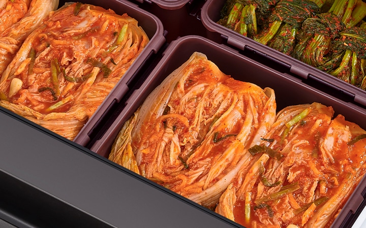 김치가 담긴 여러 개의 용기가 보입니다. 배추김치와 갓김치가 각각 용기에 정리되어 있습니다. 김치는 빨간 양념이 고루 묻어 있으며, 배추김치는 길게 절여져 있고 갓김치는 짧게 잘려 있습니다. 용기는 깔끔하게 정돈되어 있는 모습입니다.