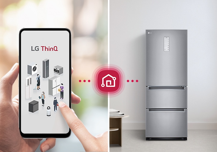 스마트폰 화면에 LG ThinQ라는 텍스트와 함께 다양한 가전제품 아이콘이 표시되어 있습니다. 손가락이 화면을 터치하고 있으며, 화면과 연결된 빨간색 집 아이콘이 있습니다. 배경에는 회색 냉장고가 놓여 있고, 옆에 작은 테이블과 접힌 수건이 있습니다. 창가에는 식물이 장식되어 있습니다.