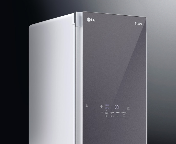 LG Styler라는 글자가 있는 가전제품의 일부가 보입니다. 제품의 전면은 어두운 색상으로 되어 있으며, 디지털 디스플레이와 터치 버튼이 있습니다. 배경은 어두운 색상으로 제품을 강조하고 있습니다.