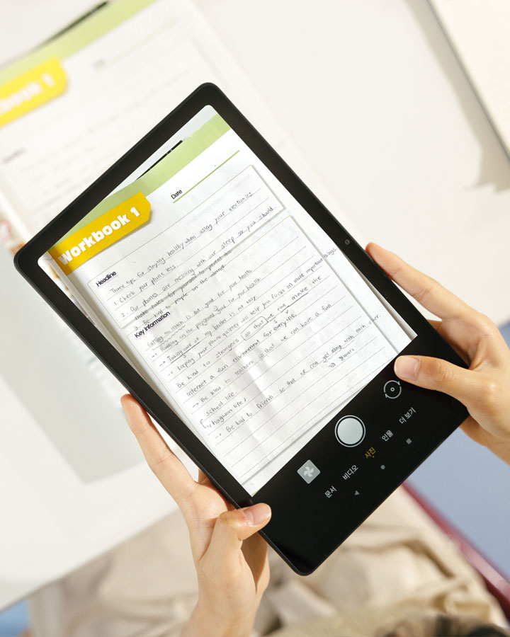 태블릿을_손으로_잡고_있으며,_화면에는_workbook_1이라는_제목의_노트가_보입니다._노트에는_headline,_tips_for_sleeping_easily_when_using_your_electronic_device,_key_information_등의_텍스트가_포함되어_있습니다._태블릿_하단에는_문서,_비디오,_사진,_입력,_더보기_등의_버튼이_있습니다._배경에는_흐릿한_책이_보입니다.