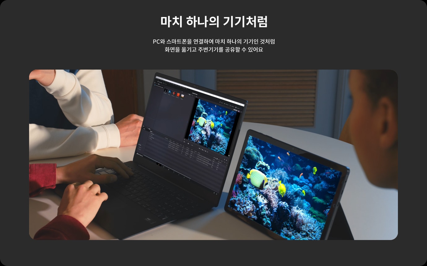마치 하나의 기기처럼. PC와 스마트폰을 연결하여 마치 하나의 기기인 것처럼 화면을 옮기고 주변기기를 공유할 수 있어요. 두 사람이 테이블에 앉아 노트북과 태블릿을 사용하고 있으며, 두 기기 모두 산호초와 열대어가 있는 바다 사진을 보여주고 있습니다.