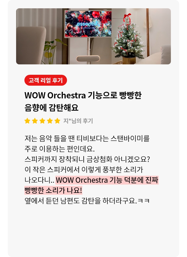 스탠바이미 스피커 제품에 대한 리뷰 컨텐츠입니다. 리뷰 사진에는 스탠바이미 제품과 스피커가 보입니다. 스탠드 위 화면에서는 'essential'이라는 문구가 보이고 빨간색과 은색 공, 금색 리본으로 장식된 크리스마스 트리가 가득하며, 반짝이는 조명도 보입니다. 스탠바이미 아래에는 둥근 베이지색 스피커가 놓여 있습니다. 오른쪽에는 빨간 리본과 전구가 감긴 크리스마스 트리가 놓여 있으며, 나무 아래에는 금색 화분이 보입니다. 전체적으로 따뜻하고 축제 분위기가 느껴지는 장면입니다. 상세내용은 하단 참고.