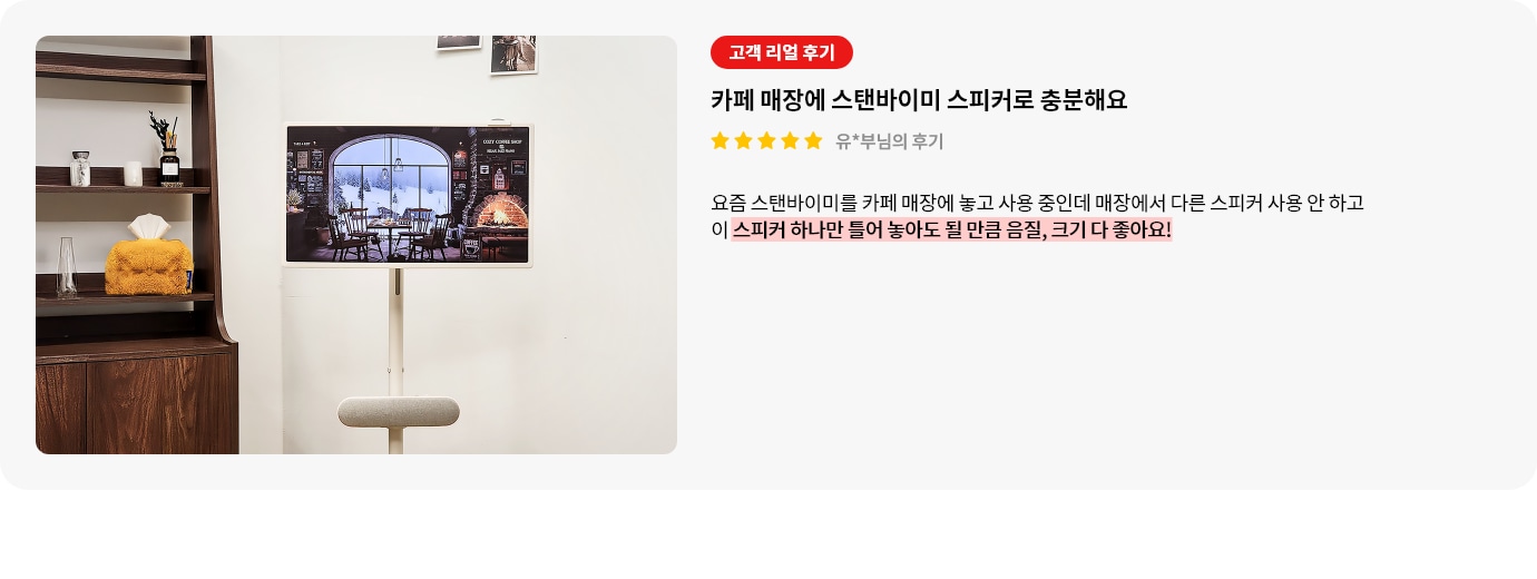 스탠바이미 스피커 제품에 대한 리뷰 컨텐츠입니다. 리뷰 사진에는 스탠바이미 제품과 스피커가 보입니다. 화면에는 창문 밖으로 눈 내리는 풍경이 보이는 아늑한 카페 내부가 그려져 있습니다. 벽난로에는 불이 지펴져 있고, 따뜻한 조명들이 보입니다. TV 아래에는 길고 둥근 베이지색 스피커가 놓여 있습니다. 왼쪽에는 나무색 책장이 있으며, 그 위에 책과 장식품들이 진열되어 있습니다. 상세내용은 하단 참고.