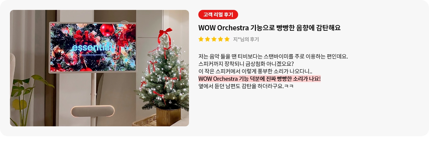 스탠바이미 스피커 제품에 대한 리뷰 컨텐츠입니다. 리뷰 사진에는 스탠바이미 제품과 스피커가 보입니다. 스탠드 위 화면에서는 'essential'이라는 문구가 보이고 빨간색과 은색 공, 금색 리본으로 장식된 크리스마스 트리가 가득하며, 반짝이는 조명도 보입니다. 스탠바이미 아래에는 둥근 베이지색 스피커가 놓여 있습니다. 오른쪽에는 빨간 리본과 전구가 감긴 크리스마스 트리가 놓여 있으며, 나무 아래에는 금색 화분이 보입니다. 전체적으로 따뜻하고 축제 분위기가 느껴지는 장면입니다. 상세내용은 하단 참고.