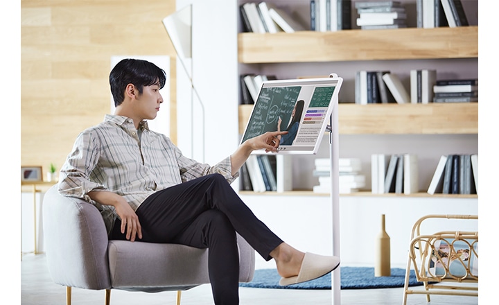 남성이 의자에 앉아 화면을 터치하고 있습니다. 화면에는 수학 공식과 그래프가 표시되어 있으며, 배경에는 책이 꽂힌 책장이 보입니다. 실내는 현대적인 분위기를 연출하고 있습니다.