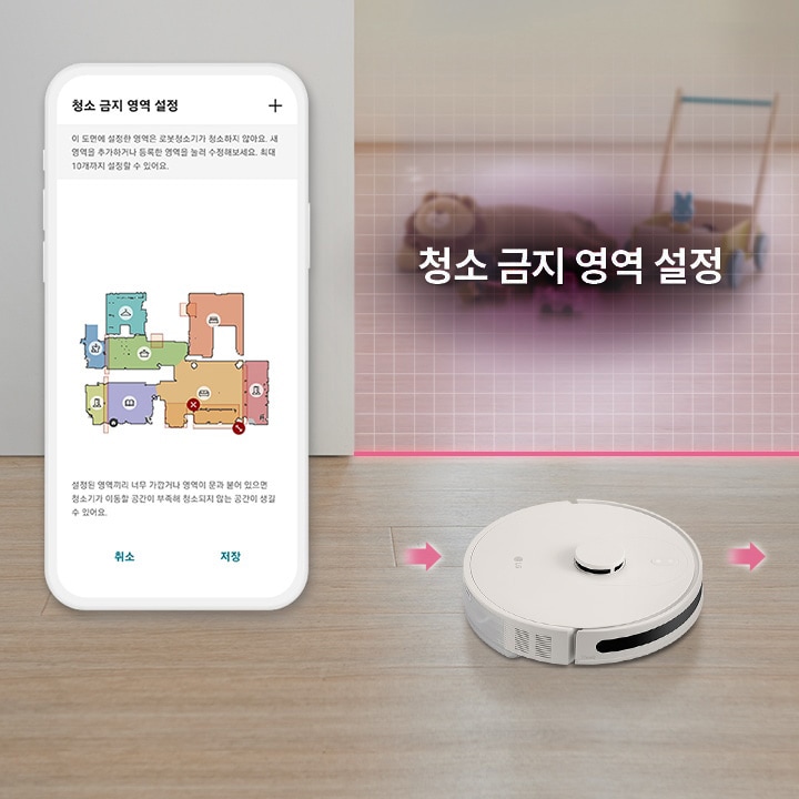 스마트폰_화면에는_청소_금지_영역_설정이라는_제목과_함께_다양한_색상으로_구분된_집의_평면도가_보이며,_설정_방법에_대한_설명이_있습니다._설명은_이_도면에_설정한_영역은_로봇청소기가_청소하지_않아요._사용자를_추가하거나_원하는_영역을_크게_수정해주세요._최대_10개까지_설정할_수_있어요.라는_내용입니다._취소와_저장_버튼이_있습니다._바닥에는_로봇청소기가_있으며,_청소_금지_영역_설정이라는_문구가_배경에_표시되어_있습니다.