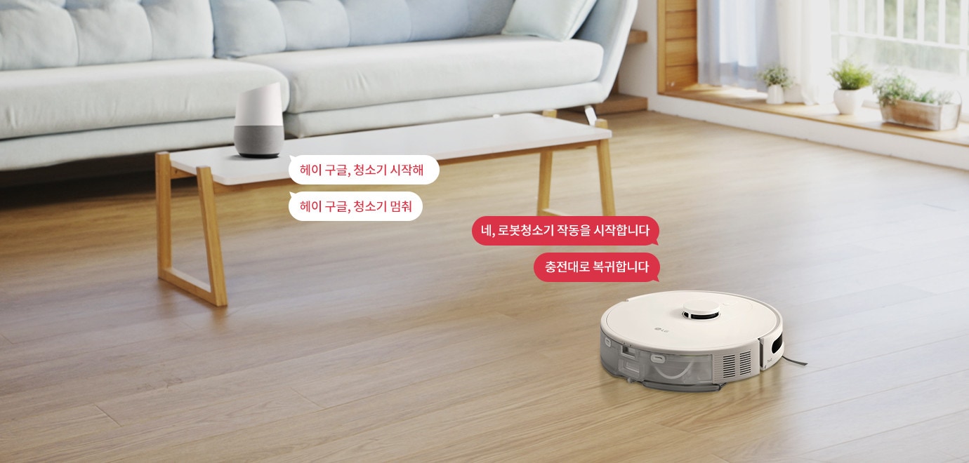 거실에 로봇청소기와 스마트 스피커가 있는 장면입니다. 스마트 스피커 옆에는 헤이 구글, 청소기 시작해와 헤이 구글, 청소기 멈춰라는 텍스트가 있습니다. 로봇청소기 옆에는 네, 로봇청소기 작동을 시작합니다와 충전대로 복귀합니다라는 텍스트가 있습니다. 바닥은 나무로 되어 있으며, 창가에는 식물이 놓여 있습니다.