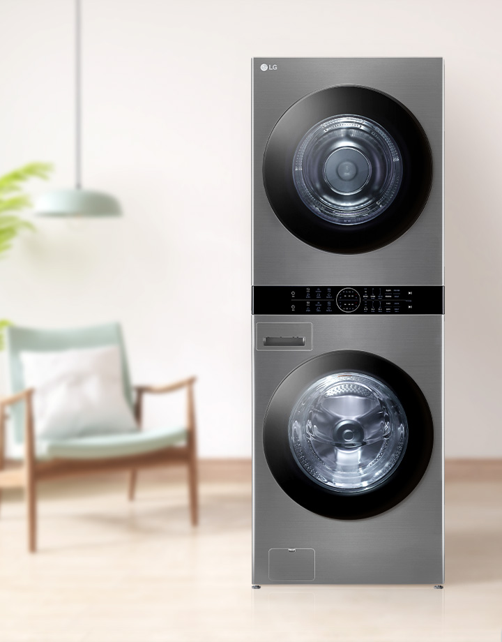 세련된 디자인의 스테인리스 스틸 세탁기와 건조기가 위아래로 쌓여 있으며, 주변에는 식물과 의자가 있는 깔끔한 실내 공간이 배경으로 보입니다. 세탁기와 건조기 사이에는 조작 패널이 위치해 있습니다.