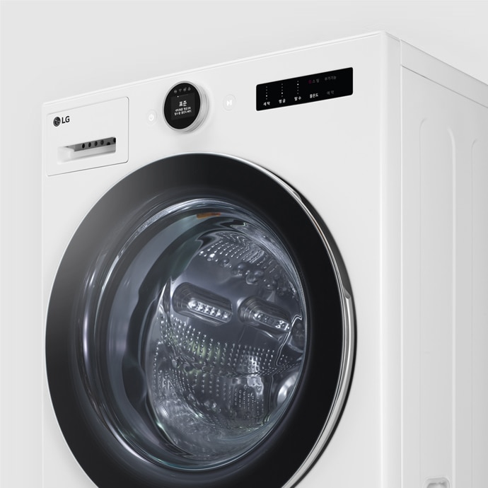 LG 트롬 세탁기가 있습니다. 세탁기의 전면에는 투명한 문이 있으며, 내부 드럼이 보입니다. 상단에는 LG 로고와 TROMM ThinQ라는 텍스트가 있습니다. 디지털 디스플레이와 조작 버튼이 함께 배치되어 있습니다.