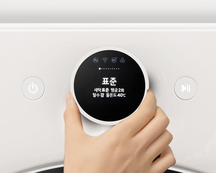 세탁기의 조작 패널이 보이며, 손이 다이얼을 돌리고 있습니다. 디스플레이에는