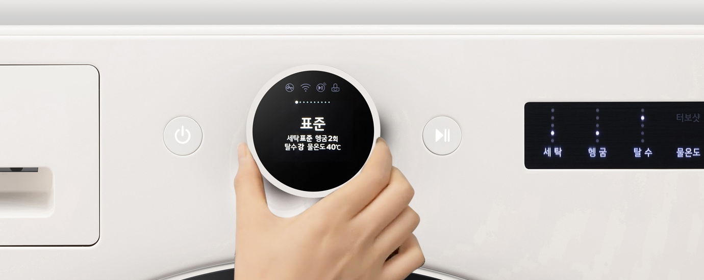 세탁기의 조작 패널이 보이며, 손이 다이얼을 돌리고 있습니다. 디스플레이에는