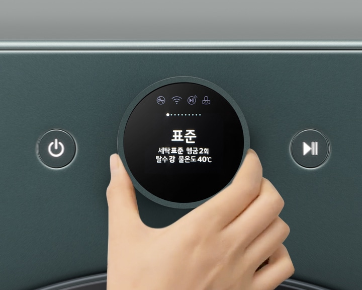 세탁기의 조작 패널이 보이며, 손이 다이얼을 돌리고 있습니다. 디스플레이에는