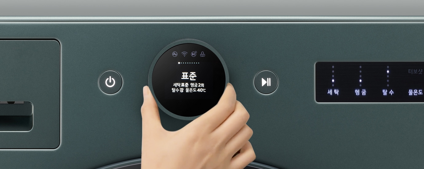 세탁기의 조작 패널이 보이며, 손이 다이얼을 돌리고 있습니다. 디스플레이에는