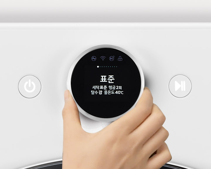 세탁기의 조작 패널을 손으로 조작하는 모습입니다. 화면에 표준이라는 글자와 함께 세탁표준 헹굼2회 탄수강 물온도40℃라는 텍스트가 표시되어 있습니다. 주변에는 전원 버튼과 세탁, 헹굼, 탈수, 물온도 등의 옵션이 있는 디스플레이가 보입니다. TROMM ThinQ 로고도 포함되어 있습니다.