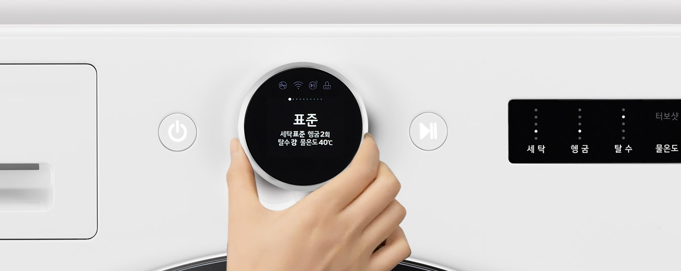 세탁기의 조작 패널을 손으로 조작하는 모습입니다. 화면에 표준이라는 글자와 함께 세탁표준 헹굼2회 탄수강 물온도40℃라는 텍스트가 표시되어 있습니다. 주변에는 전원 버튼과 세탁, 헹굼, 탈수, 물온도 등의 옵션이 있는 디스플레이가 보입니다. TROMM ThinQ 로고도 포함되어 있습니다.