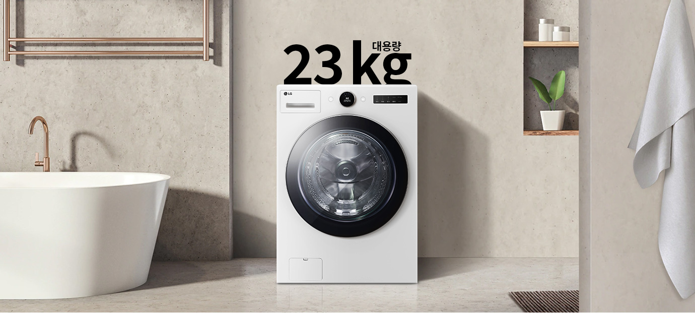 세탁기가 욕실에 놓여 있으며, 세탁기 위에는 대용량 23kg라는 글자가 있습니다. 세탁기 옆에는 욕조가 있고, 벽 선반에는 화분과 용기가 놓여 있습니다. 수건이 걸려 있는 모습도 보입니다.