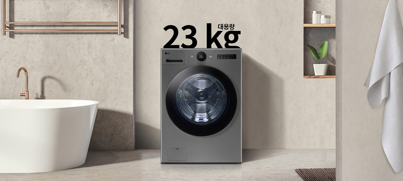 세련된 디자인의 회색 세탁기가 욕실에 놓여 있으며, 세탁기 위에는 대용량 23kg이라는 텍스트가 있습니다. 주변에는 현대적인 욕조와 수건이 걸려 있고, 벽 선반에는 화분과 용기가 놓여 있습니다.