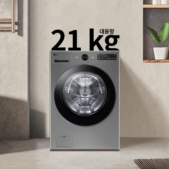 세탁기가 욕실에 놓여 있으며, 세탁기 위에는 21kg 대용량이라는 문구가 있습니다. 세탁기는 금속성 외관을 가지고 있고, 욕실에는 욕조와 수건이 걸려 있습니다. 벽에는 식물이 놓인 선반이 있습니다.