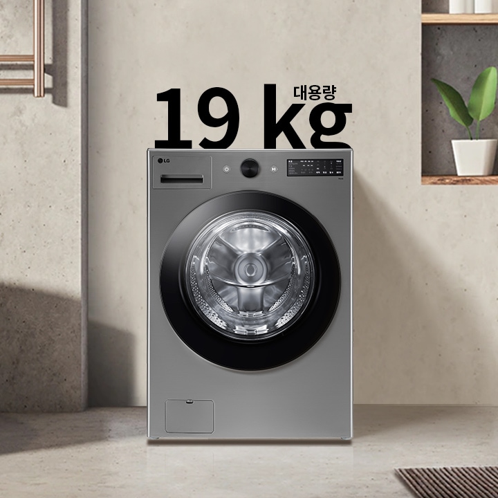 세탁기가 욕실에 놓여 있으며, 세탁기 위에는 19 kg 대용량이라는 문구가 있습니다. 세탁기 주변에는 욕조와 수건이 걸려 있고, 벽 선반에는 화분과 용기가 놓여 있습니다.