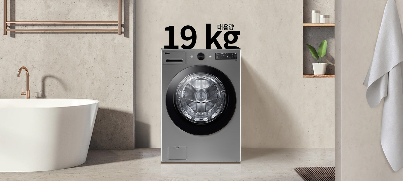 세탁기가 욕실에 놓여 있으며, 세탁기 위에는 19 kg 대용량이라는 문구가 있습니다. 세탁기 주변에는 욕조와 수건이 걸려 있고, 벽 선반에는 화분과 용기가 놓여 있습니다.